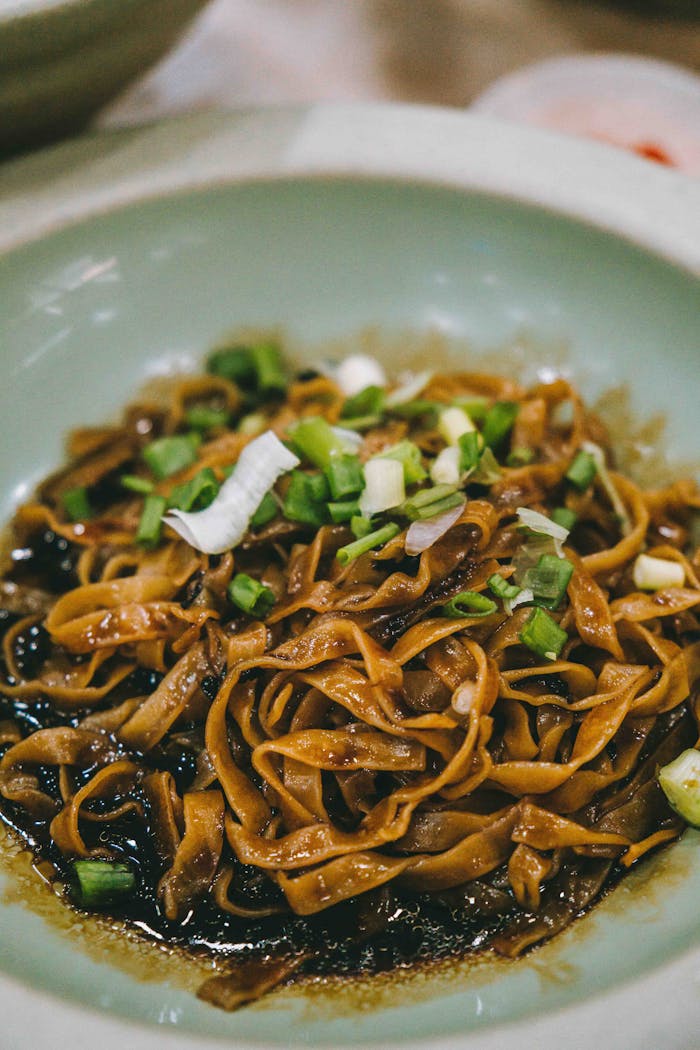Savor the flavors of a classic Asian noodle dish garnished with spring onions. A taste of Kuala Lumpur.